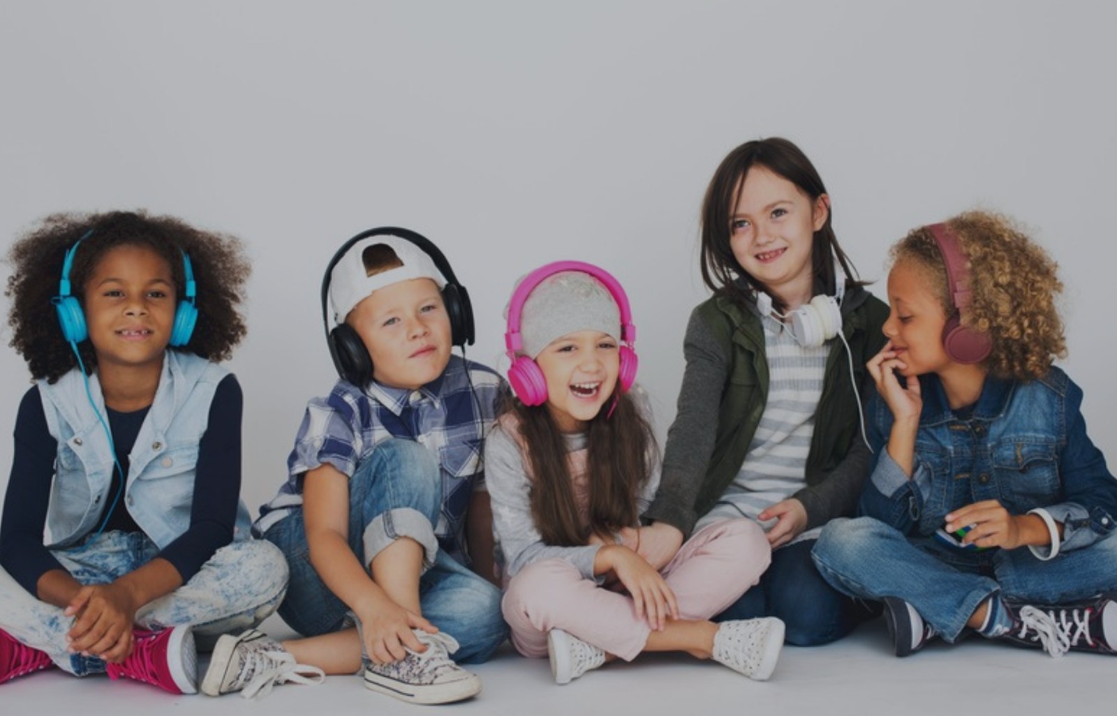 Groep van vijf kinderen met koptelefoons voor een witte studio-achtergrond