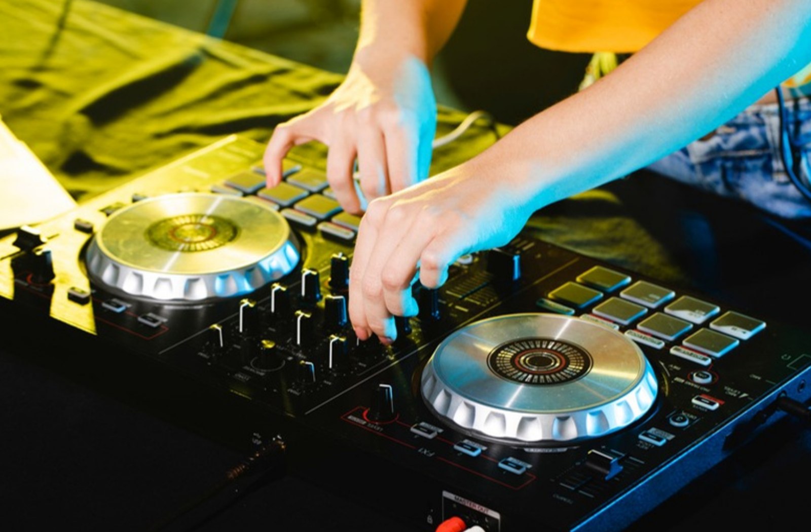 Close-up van handen op een DJ-mixer met geel-groene neonverlichting