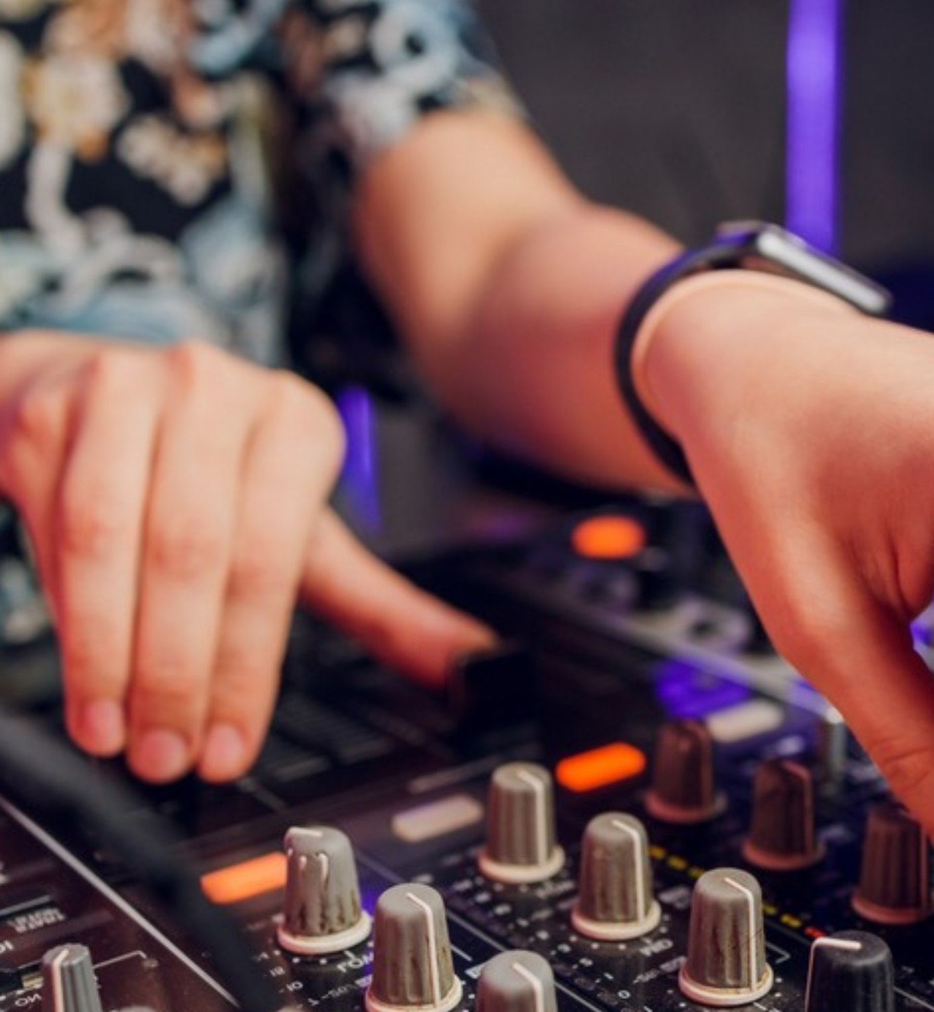 Close-up van handen op een DJ-mixer met paars-oranje verlichting